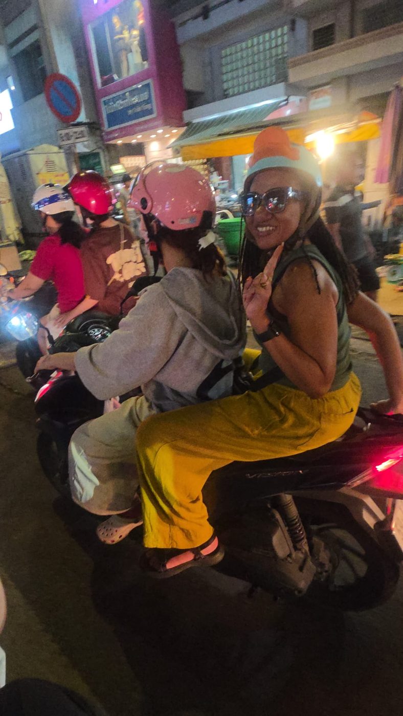 Brittney smiling on the back of a motorbike on a busy city street at night